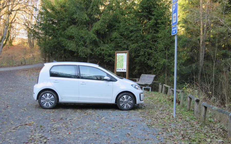 Kleines weißes Auto parkt auf Parkplatz im Wald. Kleines weißes Auto parkt auf Parkplatz im Wald.