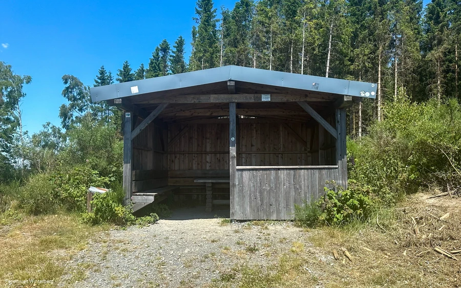 Eine Schutzhütte umgeben von Wald.